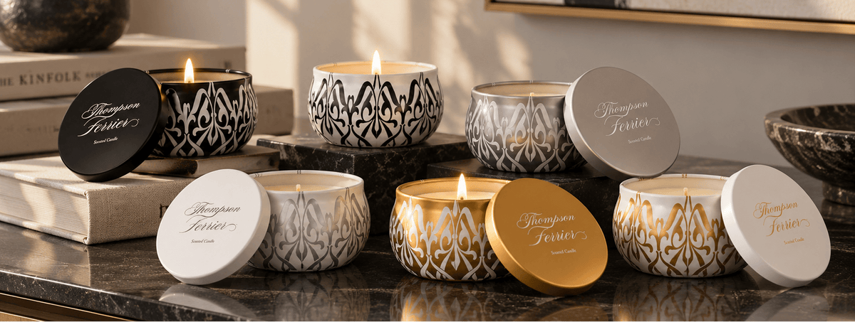 A styled arrangement of multiple lit candles in decorative patterned glass jars with matching lids, displayed on a dark marble countertop in a warm interior setting.